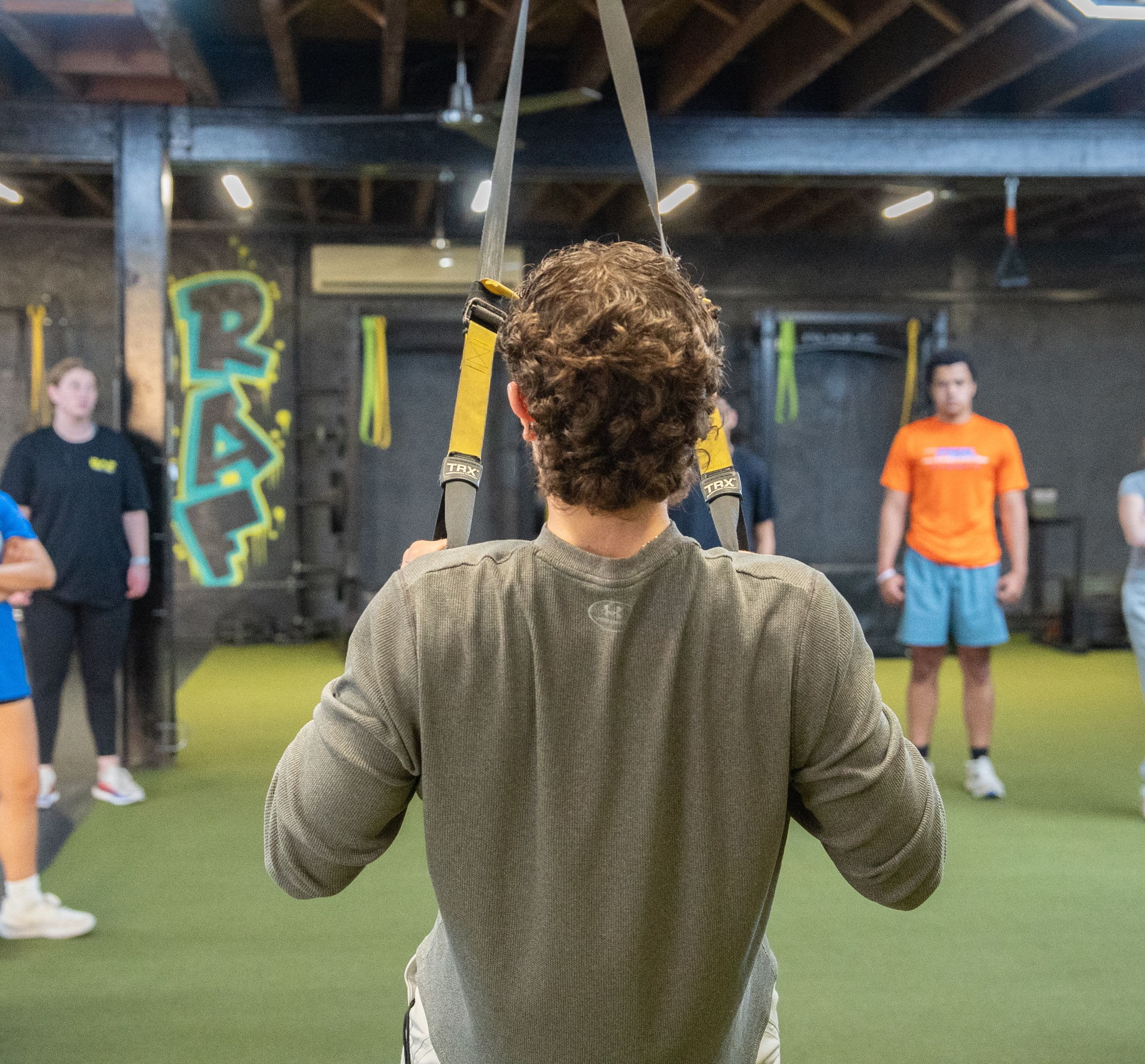 College athlete on TRX straps with RAF coaches and teammates in the background