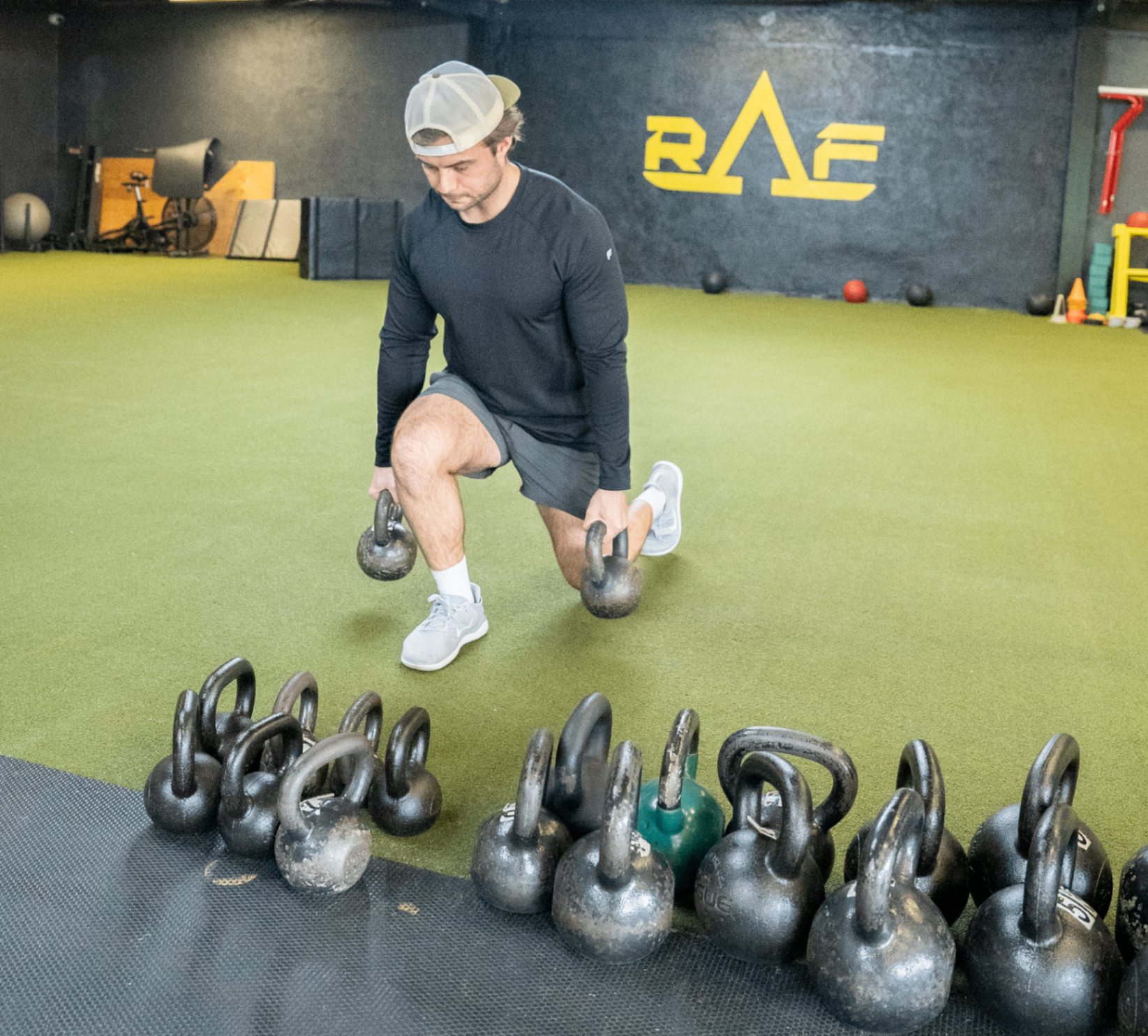 College athlete picking up kettlebells in front of the RAF logo on the turf